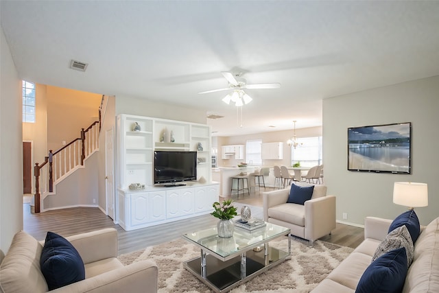 living room featuring ceiling fan with notable chandelier and light hardwood / wood-style floors