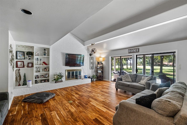 living room featuring a brick fireplace, vaulted ceiling, wood-type flooring, and built in shelves