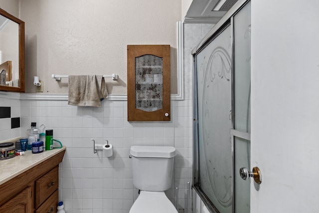 bathroom featuring tile walls, a shower with door, vanity, and toilet