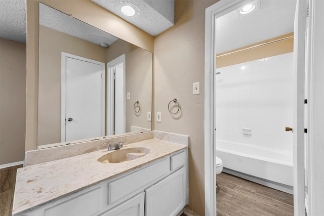 full bathroom featuring vanity, toilet, a textured ceiling, washtub / shower combination, and hardwood / wood-style floors