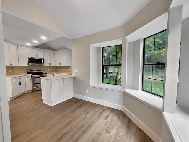 kitchen with kitchen peninsula, light hardwood / wood-style flooring, white cabinetry, appliances with stainless steel finishes, and vaulted ceiling