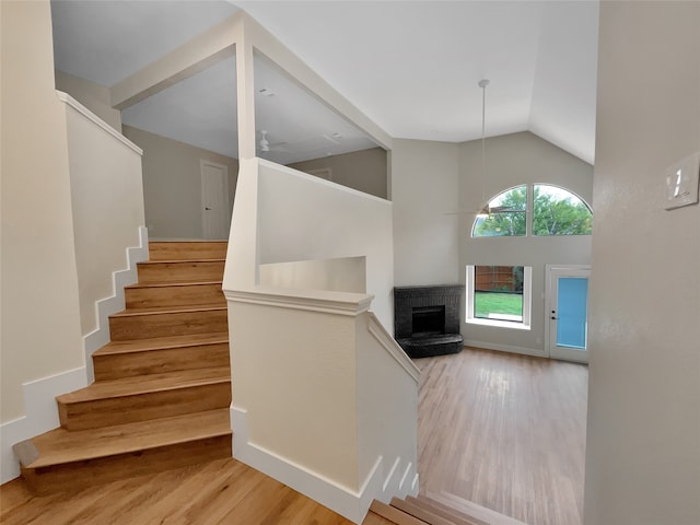 stairs with wood-type flooring, lofted ceiling, ceiling fan, and a brick fireplace