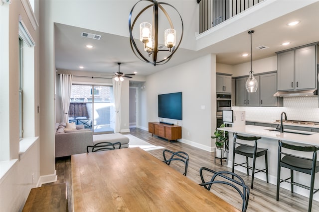 dining space with ceiling fan with notable chandelier, baseboards, visible vents, and light wood finished floors