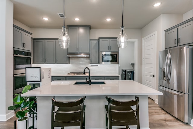 kitchen with gray cabinetry, under cabinet range hood, decorative backsplash, appliances with stainless steel finishes, and a sink