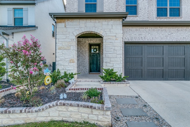 entrance to property featuring brick siding, stone siding, an attached garage, and concrete driveway