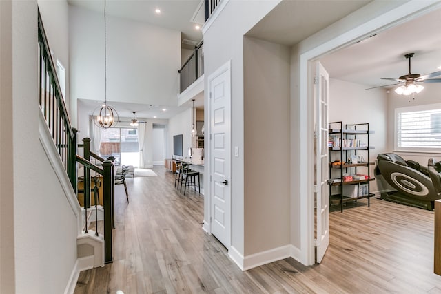 hall featuring light wood-style floors, a high ceiling, a chandelier, and stairs