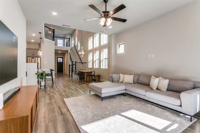 living area with stairway, ceiling fan with notable chandelier, visible vents, and light wood finished floors