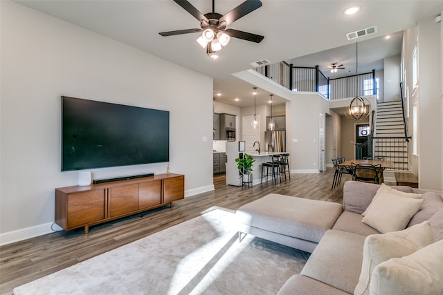 living room with stairway, baseboards, wood finished floors, and ceiling fan with notable chandelier