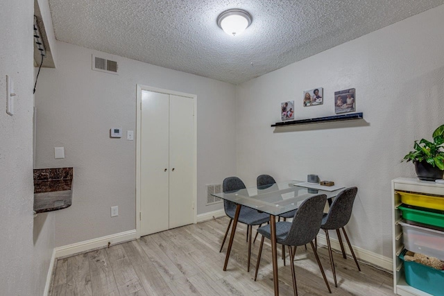 dining room with light wood-type flooring and a textured ceiling