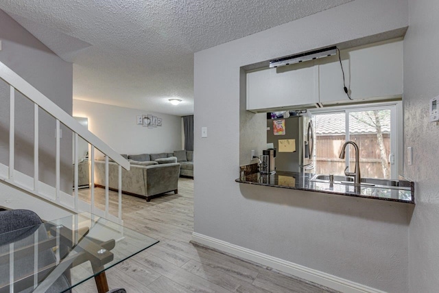 interior space featuring sink, a textured ceiling, light hardwood / wood-style flooring, white cabinetry, and stainless steel refrigerator