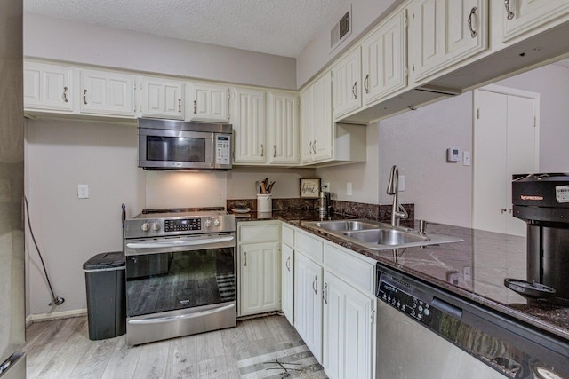 kitchen featuring dark stone counters, light hardwood / wood-style floors, a textured ceiling, sink, and stainless steel appliances