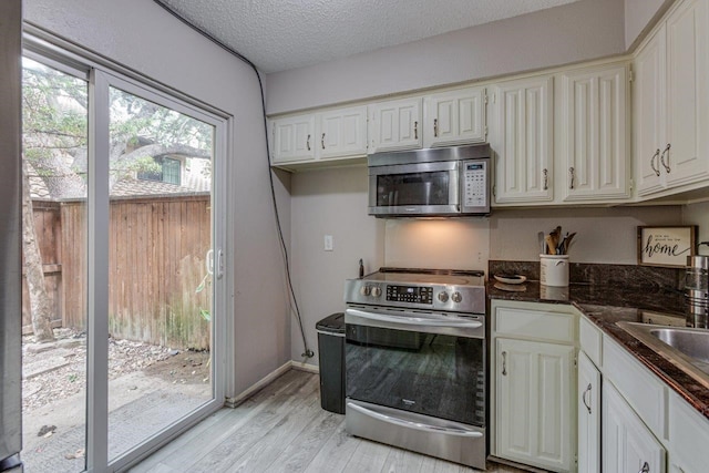 kitchen with light wood-type flooring, a textured ceiling, stainless steel appliances, and white cabinets