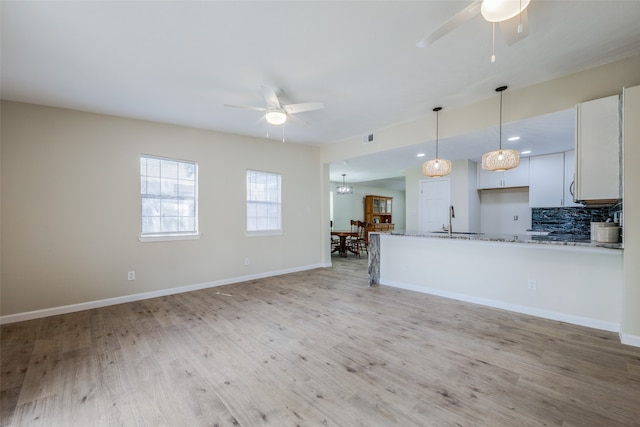 kitchen with light stone countertops, ceiling fan, light hardwood / wood-style floors, decorative backsplash, and white cabinets