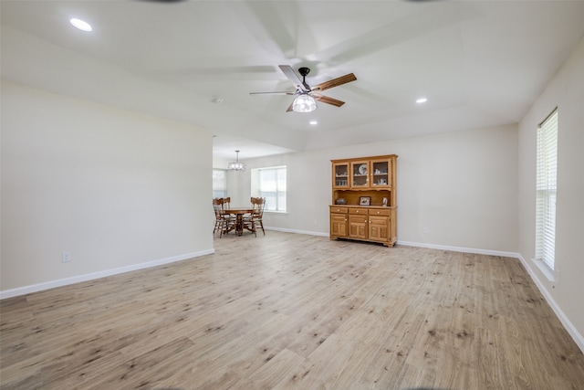 unfurnished living room with ceiling fan with notable chandelier and light wood-type flooring