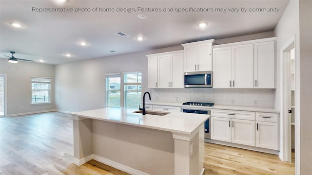 kitchen with appliances with stainless steel finishes, tasteful backsplash, sink, white cabinetry, and an island with sink