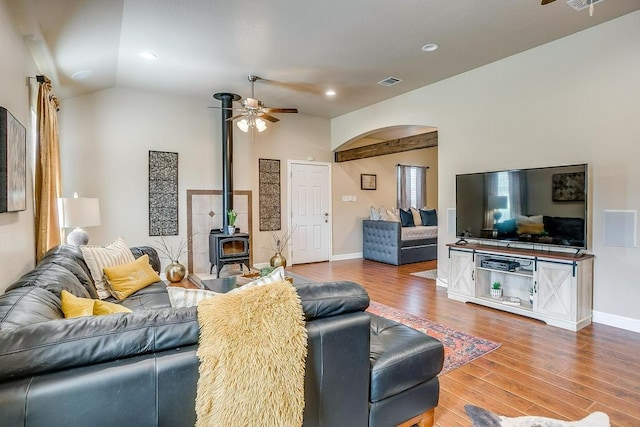 living room featuring lofted ceiling, ceiling fan, a wood stove, and hardwood / wood-style flooring