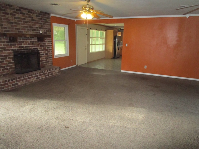 unfurnished living room featuring ceiling fan, light colored carpet, a brick fireplace, and crown molding