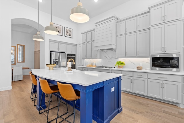 kitchen with a breakfast bar area, appliances with stainless steel finishes, an island with sink, and hanging light fixtures