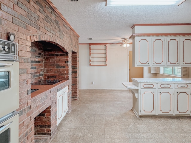 kitchen with ornamental molding, white cabinets, ceiling fan, and a textured ceiling