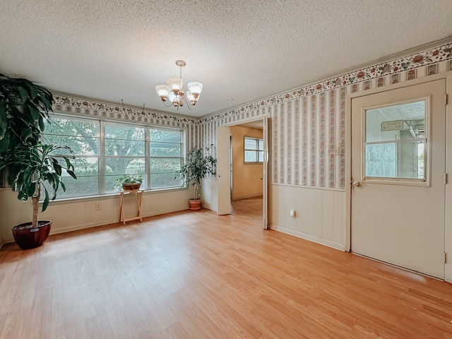 empty room featuring a textured ceiling, an inviting chandelier, and light hardwood / wood-style flooring