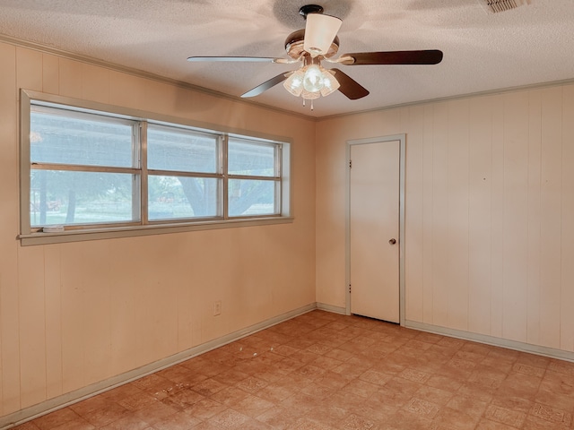 spare room featuring wooden walls, ceiling fan, and a textured ceiling