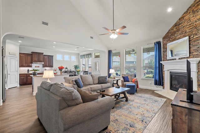 living room featuring a stone fireplace, light hardwood / wood-style flooring, ceiling fan, and plenty of natural light