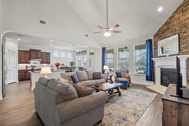 living area with high vaulted ceiling, a large fireplace, light wood-style floors, visible vents, and a ceiling fan