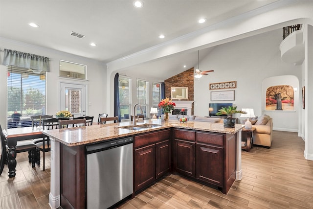 kitchen with dishwasher, a large fireplace, ceiling fan, a center island with sink, and sink