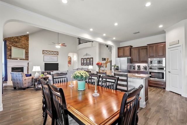 dining space featuring ornamental molding, a large fireplace, ceiling fan, and dark hardwood / wood-style floors