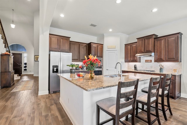 kitchen featuring light stone counters, dark wood-type flooring, a kitchen island with sink, sink, and stainless steel appliances