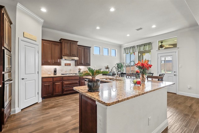 kitchen featuring hardwood / wood-style floors, crown molding, a kitchen island with sink, and sink