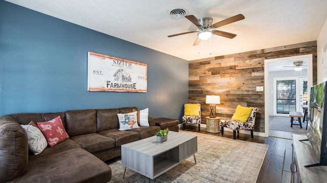 living room with wooden walls, ceiling fan, and hardwood / wood-style flooring