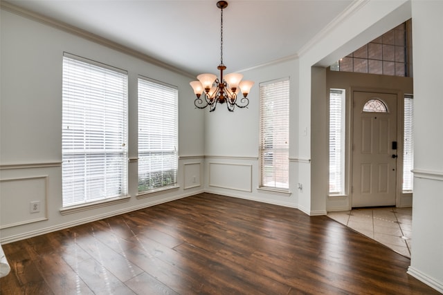 foyer entrance featuring an inviting chandelier, dark hardwood / wood-style floors, crown molding, and a wealth of natural light