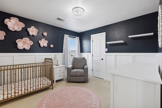 carpeted bedroom featuring a textured ceiling and a nursery area