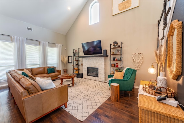 living room with high vaulted ceiling, dark wood-type flooring, a healthy amount of sunlight, and a stone fireplace