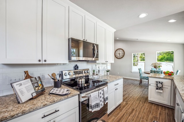 kitchen featuring dark wood-type flooring, lofted ceiling, white cabinetry, appliances with stainless steel finishes, and light stone countertops