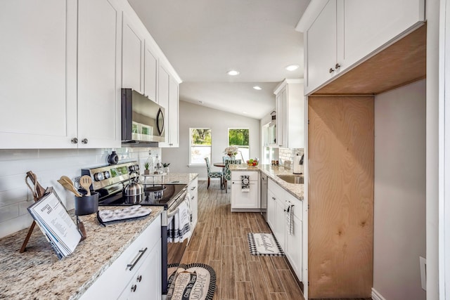 kitchen featuring white cabinets, lofted ceiling, appliances with stainless steel finishes, and light stone counters