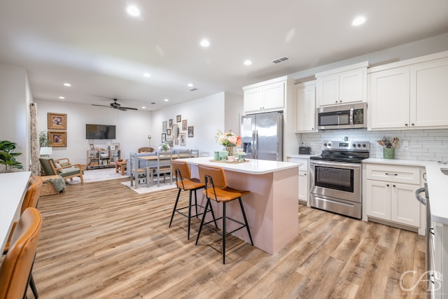 kitchen with a kitchen island, white cabinetry, appliances with stainless steel finishes, a breakfast bar area, and light hardwood / wood-style floors