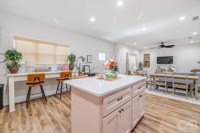 kitchen featuring a breakfast bar, light hardwood / wood-style floors, white cabinets, a kitchen island, and ceiling fan