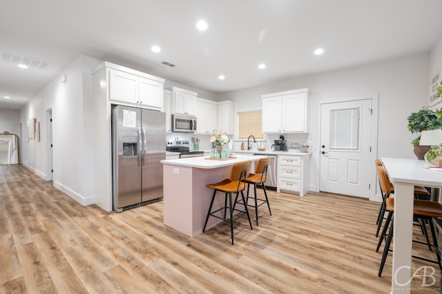 kitchen featuring a kitchen bar, a kitchen island, light hardwood / wood-style flooring, stainless steel appliances, and backsplash