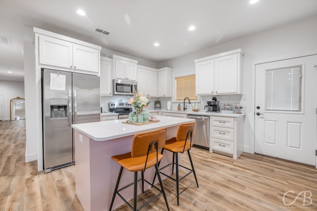 kitchen with appliances with stainless steel finishes, a kitchen island, light hardwood / wood-style flooring, and white cabinetry