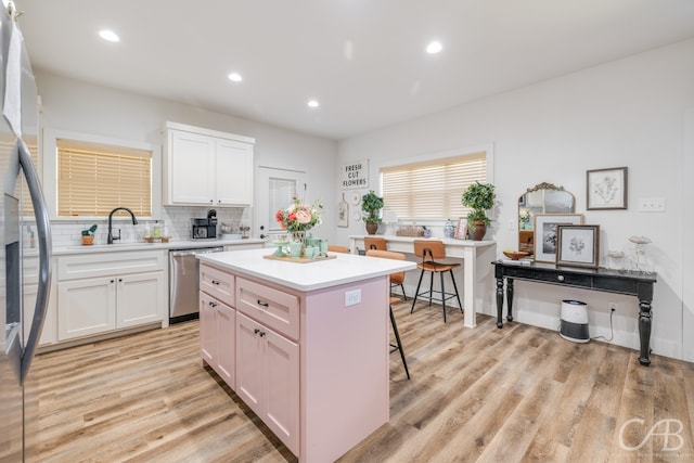 kitchen featuring a kitchen breakfast bar, white cabinetry, a kitchen island, stainless steel appliances, and light wood-type flooring