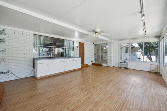 unfurnished living room featuring light wood-type flooring, ceiling fan, and brick wall