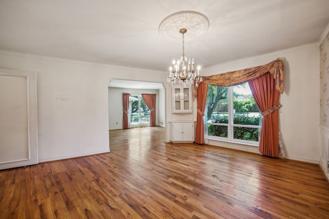 spare room with a healthy amount of sunlight, crown molding, an inviting chandelier, and wood-type flooring