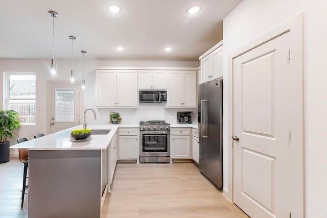 kitchen with decorative light fixtures, premium appliances, sink, a kitchen breakfast bar, and kitchen peninsula