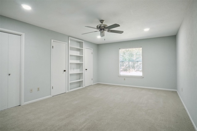 unfurnished bedroom featuring ceiling fan, light colored carpet, and multiple closets