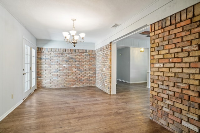 spare room with a notable chandelier, wood-type flooring, brick wall, and ornamental molding