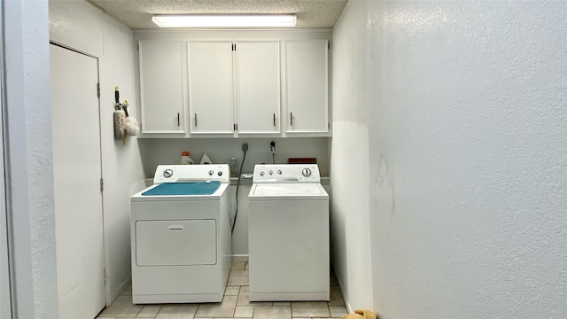 laundry area with washing machine and dryer, light tile patterned floors, cabinets, and a textured ceiling