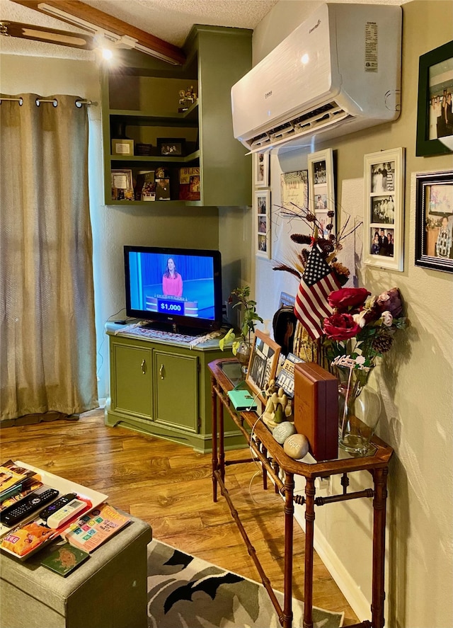 living room featuring beamed ceiling, a textured ceiling, a wall unit AC, and light hardwood / wood-style flooring