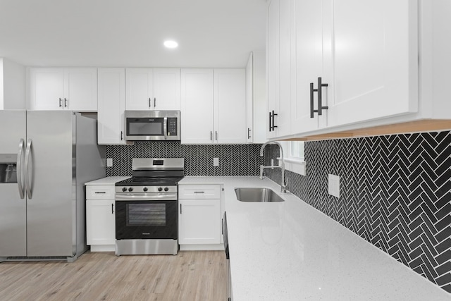 kitchen with white cabinets, sink, tasteful backsplash, stainless steel appliances, and light hardwood / wood-style floors